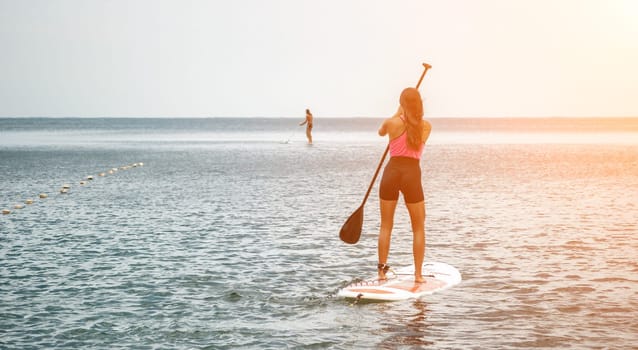 Sea woman and man on sup. Silhouette of happy young woman and man, surfing on SUP board, confident paddling through water surface. Idyllic sunset. Active lifestyle at sea or river
