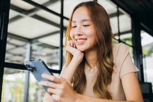 Beautiful Asian female has transfer money financial internet banking on mobile phone, young woman using smart phone for shopping online at cafe coffee shop near windows in the morning