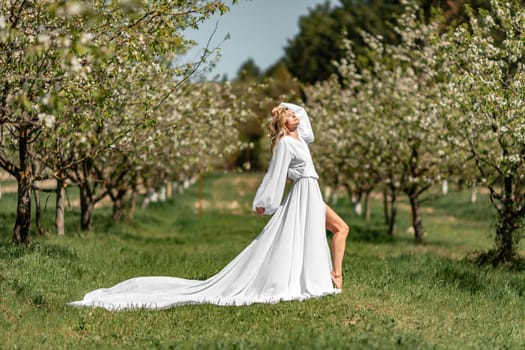 Blond blooming garden. A woman in a white dress walks through a blossoming cherry orchard. Long dress flies to the sides