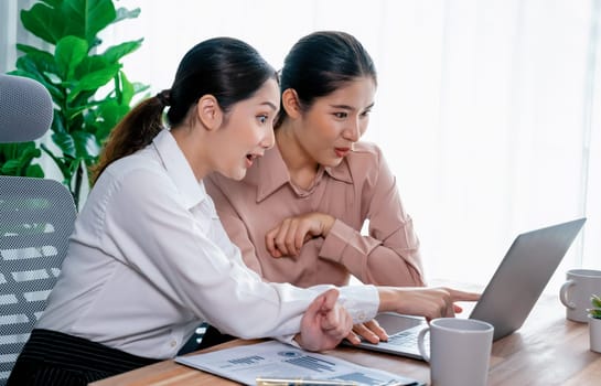 Two young office lady colleagues collaborating in modern office workspace, engaging in discussion and working together on laptop, showcasing their professionalism as modern office worker. Enthusiastic