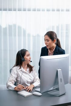 Asian female customer support operator wearing headset is guided by her supportive manager. Experienced colleague help operator handle a call with a client, providing advice and guidance. Enthusiastic