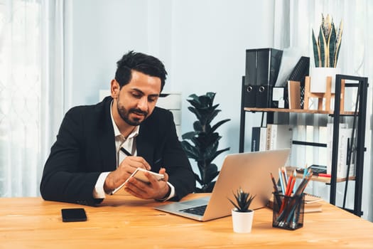 Modern professional businessman at modern office desk using laptop to work and write notes. Diligent office worker working on computer notebook in his office work space. fervent