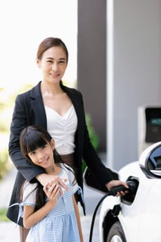 Progressive lifestyle of mother and daughter who have just returned from school in an electric vehicle that is being charged at home. Electric vehicle powered by sustainable clean energy.