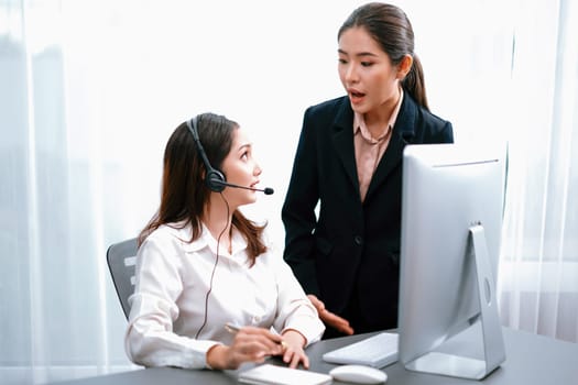 Asian female customer support operator wearing headset is guided by her supportive manager. Experienced colleague help operator handle a call with a client, providing advice and guidance. Enthusiastic