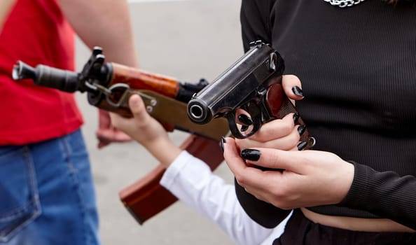 Children's hands on a rifle or machine gun. Rifle barrel. The girl is holding a Makarov pistol in her hands.