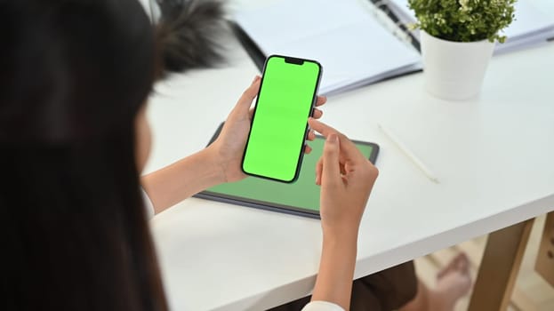 Cropped shot woman holding smartphone with green chrome screen on office desk. High quality photo
