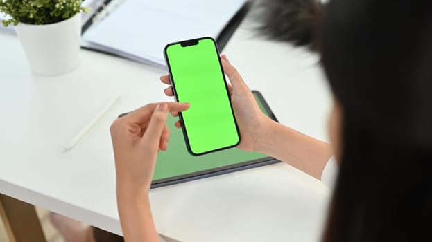 Cropped shot woman holding smartphone with green chrome screen on office desk. High quality photo