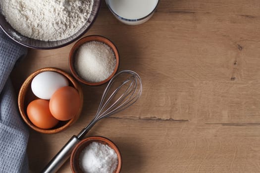 Preparation for baking. Eggs, sugar, milk, flour, salt, rolling pin, whisk on the kitchen table. copy space