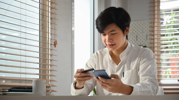 Happy asian man holding credit card and smartphone, shopping online or doing online banking transaction.