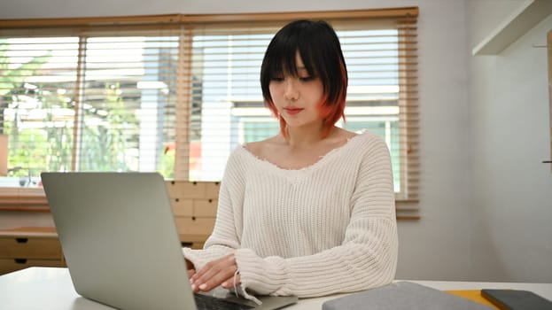 Pretty young woman using laptop computer at home. Freelance, distance, education, e-learning concept.