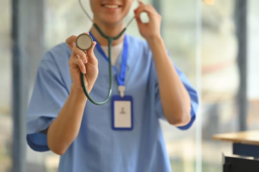 Selective focus on hand of doctor in blue scrubs holding stethoscope. Healthcare and medical concept.