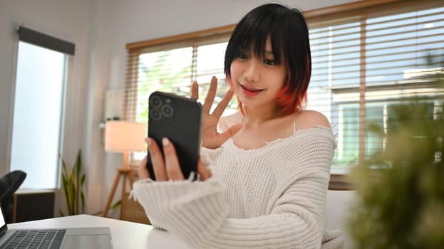 Image of pretty young asian woman waving hand, making video call, chatting online on mobile phone.