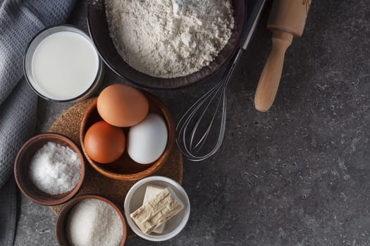 Preparation for baking. Eggs, sugar, milk, flour, salt, yeast, rolling pin, whisk on the kitchen table. copy space