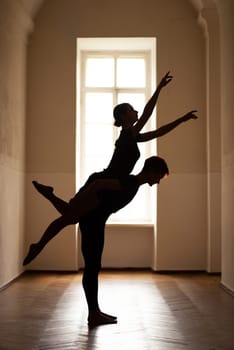 Silhouette of male and female dancers performing difficult artistic moves in corridor of theatre