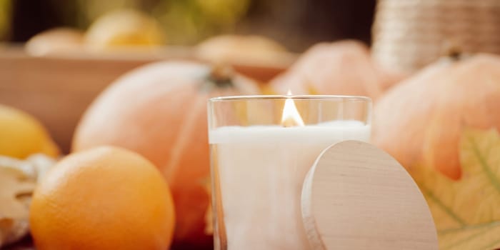 Wide photo of burning candle with autumn background of pumpkins, oranges, bright leaves