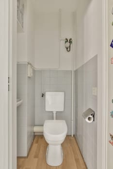 a toilet in the corner of a room with white tiles on the walls, and wood flooring around it