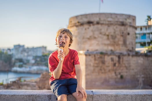 Boy tourist eating turkish ice cream on background of Hidirlik Tower in Antalya against the backdrop of the Mediterranean bay of the ancient Kaleici district, Turkey. Turkiye.