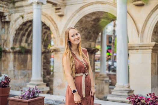 Happy female tourist traveler discover interesting places and popular attractions and walks in the old city of Antalya. Hadrian Kapisi turkey landmark city history. Popular tourist attraction - ancient Roman Hadrian Gate in old town Antalya, Turkey on a summer day. Turkiye.