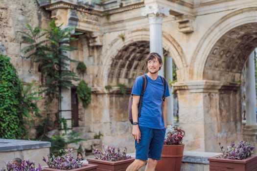 Happy male tourist traveler discover interesting places and popular attractions and walks in the old city of Antalya. Hadrian Kapisi turkey landmark city history. Popular tourist attraction - ancient Roman Hadrian Gate in old town Antalya, Turkey on a summer day. Turkiye.