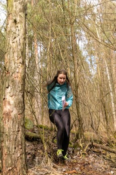Grodno, Belarus - 25 March, 2023: Strong caucasian young woman wearing sportswear running through a forest during exercise in outdoor orienteering Grodno Forest Day. Belarus, hobby sport.
