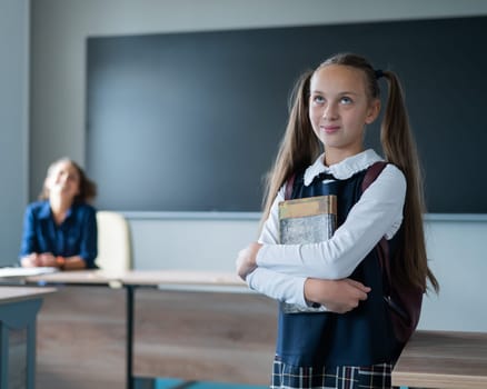 Caucasian girl and female teacher in the classroom. The schoolgirl is holding a textbook