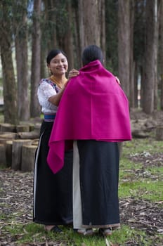 smiling indigenous girl putting a fuchsia cloak on another indigenous woman for a ritual in the forest. High quality photo