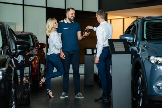 The seller hands over the car keys to the buyers. The couple bought a new car