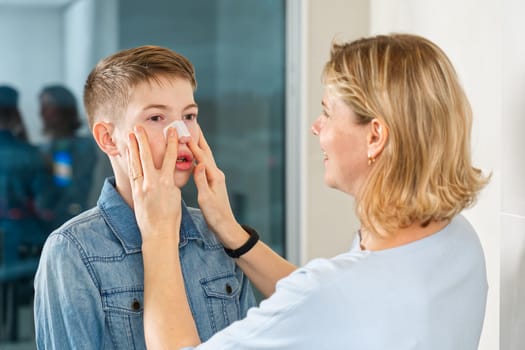 mom glues a patch to remove blackheads to her son. acne remover patch. teenage with nose band aid