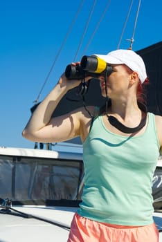 Girl on a yacht looking through binoculars. Happy female captain looks through a binoculars - marine concept