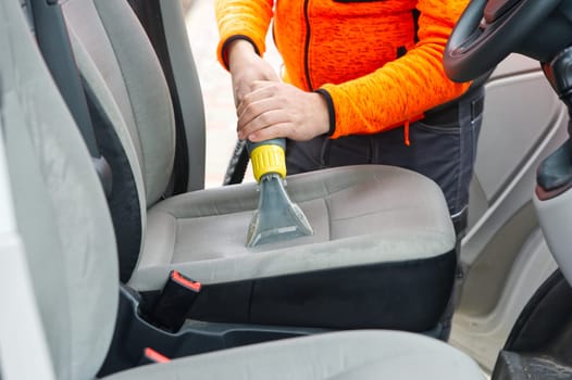 Handyman vacuuming car front textile seat with vacuum cleaner. man cleaning work Minivan.