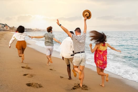 Rear view of happy multiracial group of young friends running on the beach during vacation summer. Copy space. Holiday concept.