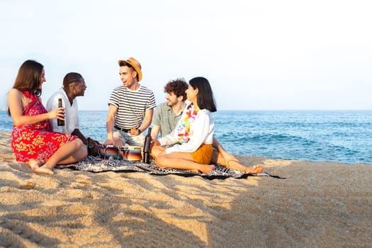 Group of multiracial having fun at the beach, talking, playing bongos and drinking beer together. Copy space. Vacation and friendship concept.