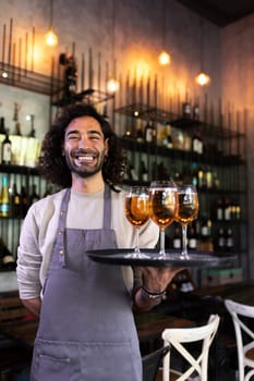 Vertical portrait of happy waiter standing in bar holding tray of beer looking at camera. Restaurant concept.