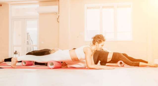 Group of young womans fitness instructor in Sportswear Leggings and Tops, stretching in the gym before pilates, on a yoga mat near the large window on a sunny day, female fitness yoga routine concept.