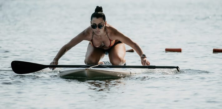 Sea woman sup. Silhouette of happy middle aged woman in rainbow bikini, surfing on SUP board, confident paddling through water surface. Idyllic sunset. Active lifestyle at sea or river