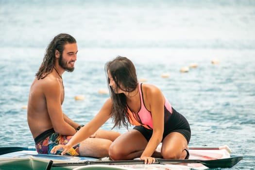 Sea woman and man on sup. Silhouette of happy young woman and man, surfing on SUP board, confident paddling through water surface. Idyllic sunset. Active lifestyle at sea or river
