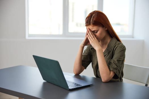 a serious, work-weary woman, with a sad face, sits at a laptop with her hands folded near her face. High quality photo