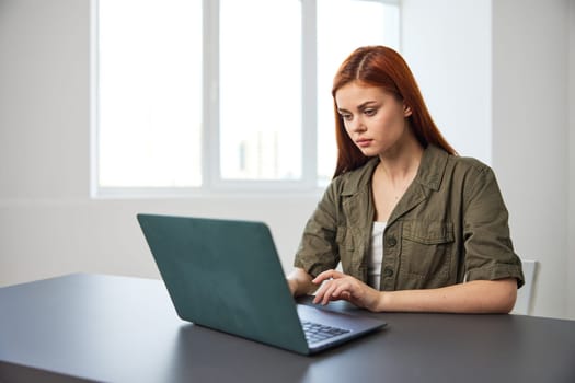 portrait of a red-haired woman in the office sitting thoughtfully at a laptop. High quality photo