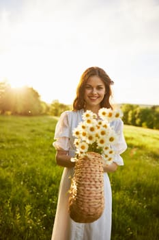 a woman in a light dress stands in a field during sunset and holds out a basket of daisies into the camera. High quality photo