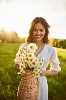 a woman in a light dress stands in a field during sunset and holds out a basket of daisies into the camera. High quality photo