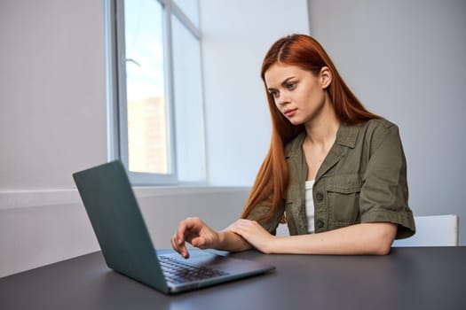 red-haired woman working in the office sitting by the window at the laptop. High quality photo