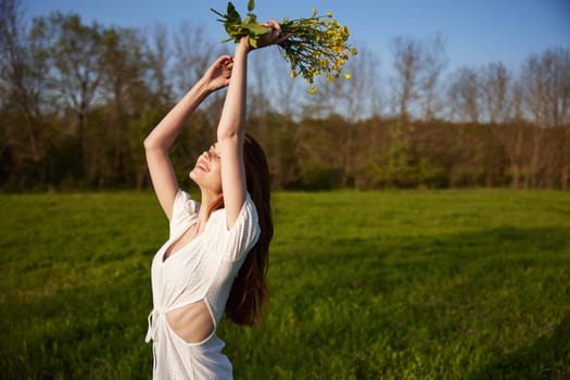 a beautiful, happy woman in a light dress stands in a field raising her hands high holding a bouquet of flowers. High quality photo