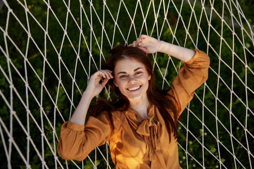 a close horizontal photo from above of a happy, pleasantly smiling woman lying on a mesh hammock in nature on a sunny day. High quality photo