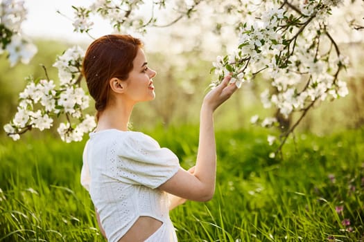 Young attractive woman with straight long hair standing in flowering Apple orchards. Beauty smiling woman looking at white flower. High quality photo