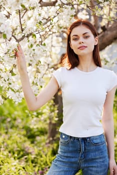 a pretty woman in casual clothes stands near a flowering tree in tall grass. High quality photo