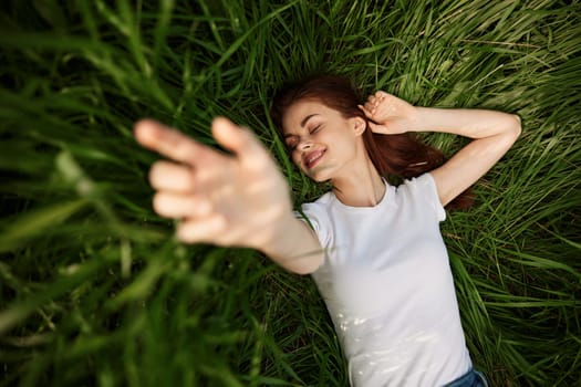 laughing redhead woman stretching her palms to the camera while lying on the grass. High quality photo