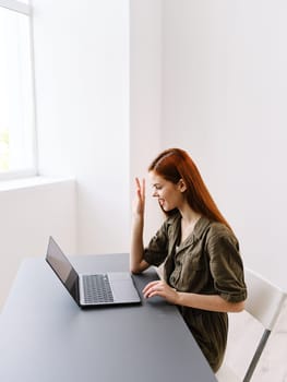 cute red-haired woman sitting at a table and working at a laptop looking seriously at the monitor. High quality photo
