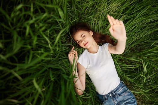 attractive teenager lying down on green grass with hands rised up to the air. High quality photo