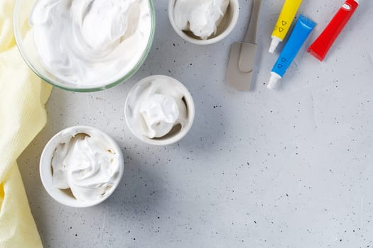 Whipped egg whites - meringue prepared for coloring in different colors, food coloring on a gray background. Copy space