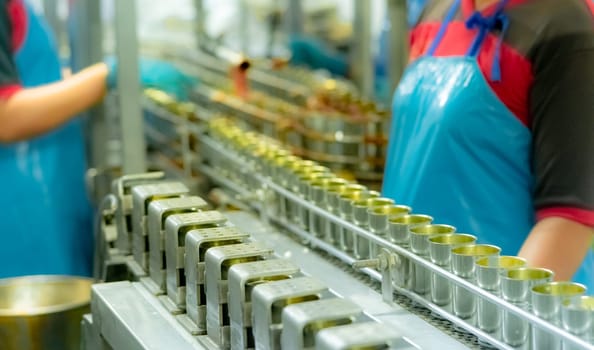 Canned fish factory. Food industry.  Sardines in red tomato sauce in tinned cans on conveyor belt at food factory. Blur workers working in food processing production line. Food manufacturing industry.